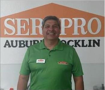 male employee wearing a green SERVPRO shirt standing in front of a SERVPRO sign